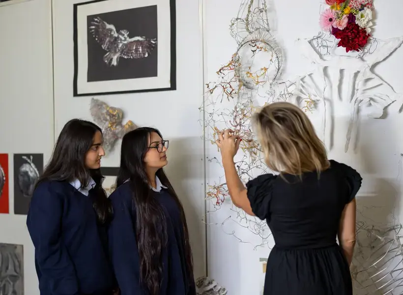 Two students and a teacher looking at and discussing artwork.